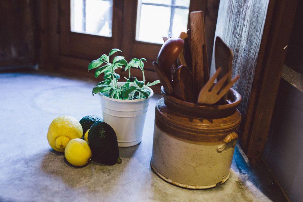 Wooden kitchen utensils in a ceramic pot beside lemons, avocados and mint.
