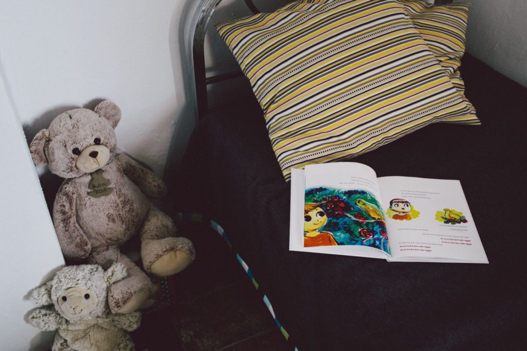 A child's bedroom with an open story book on the bed and teddy bears beside it.