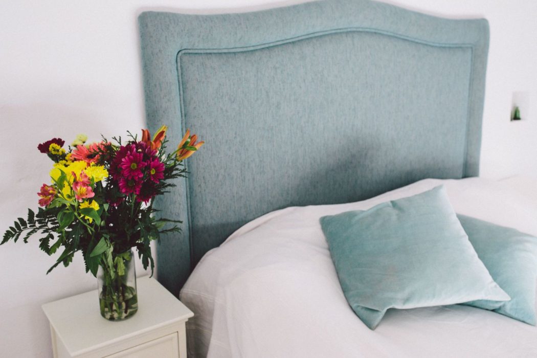 Modern bedroom with light blue linen and headboard with flowers on bedside table.