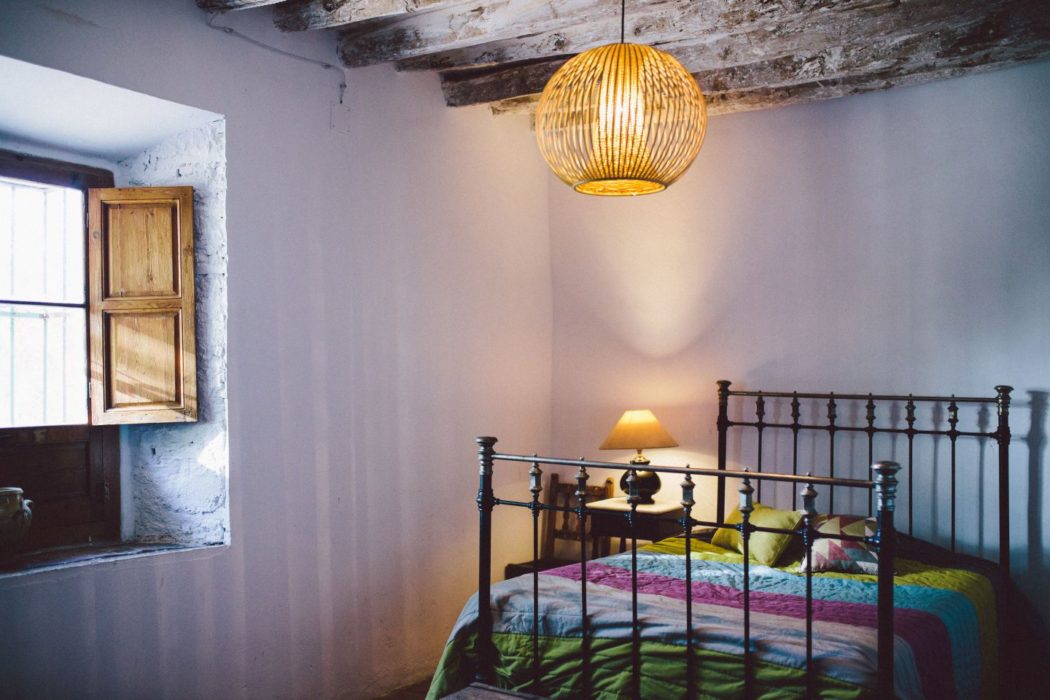 A cozy bedroom with a large lamp, wooden beams, white walls and big bedposts